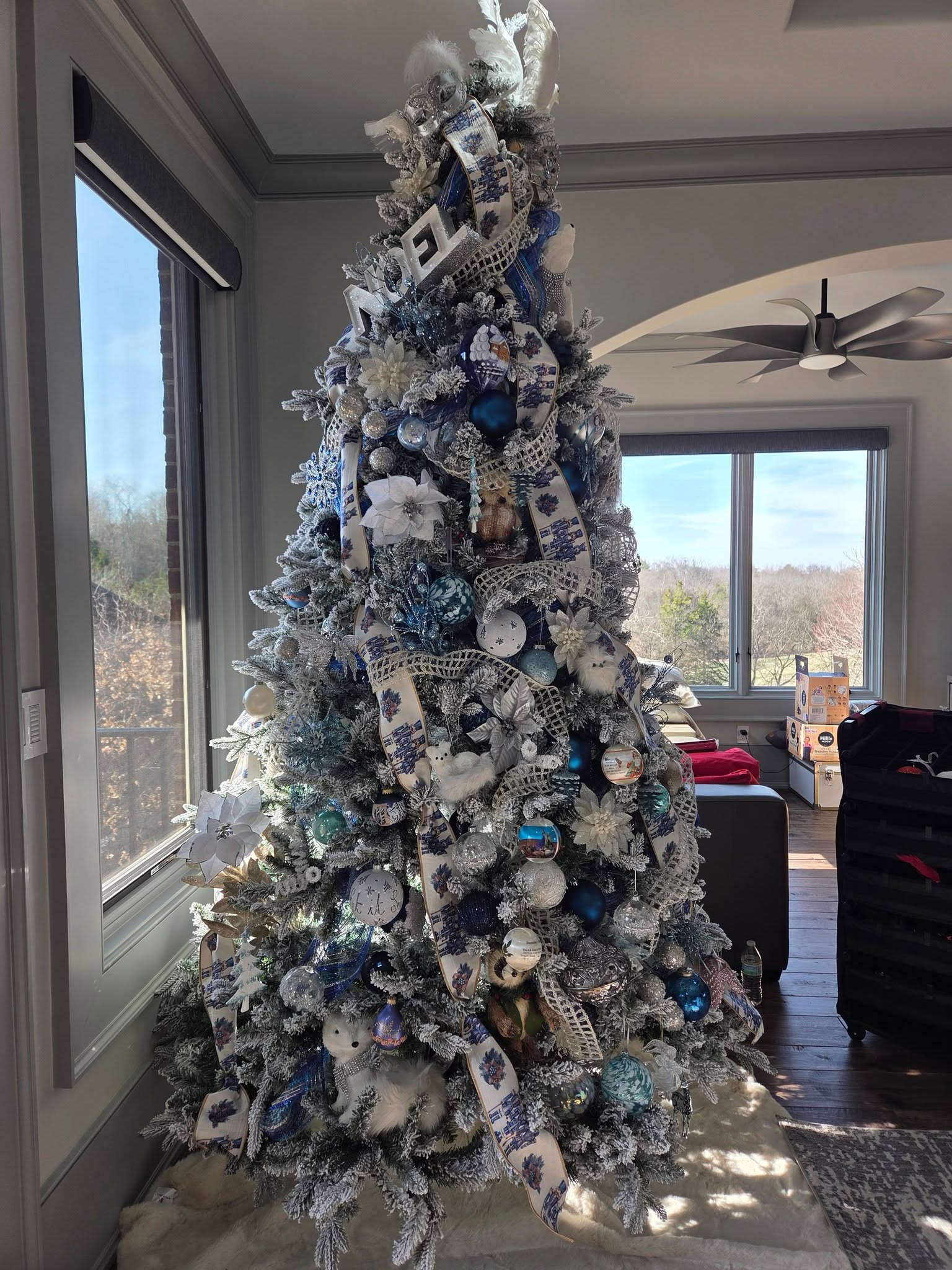 A blue and white styled Christmas tree beside tall windows